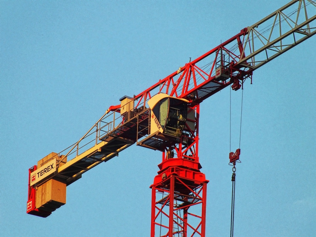 Nahaufnahme eines gelb-roten Turmdrehkrans von Terex, der die Fahrerkabine und die Gittermaststruktur vor einem blauen Himmel zeigt.