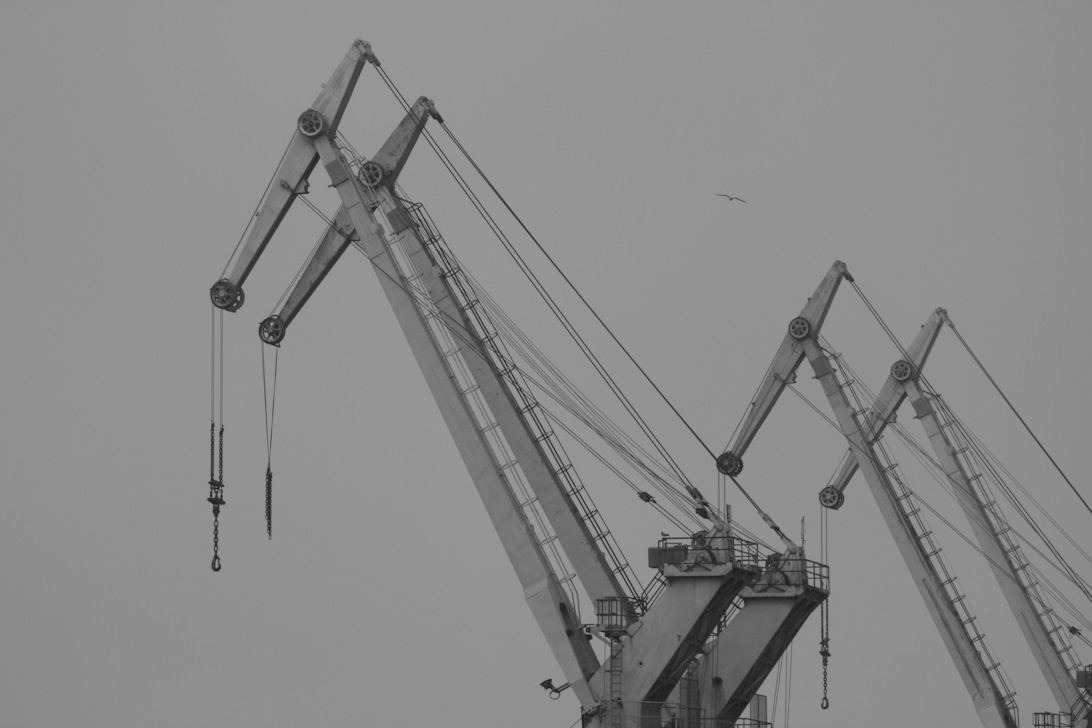 Schwarz-Weiß-Fotografie mehrerer großer Baukräne, die deren strukturelles Gerüst und mechanische Komponenten zeigen.