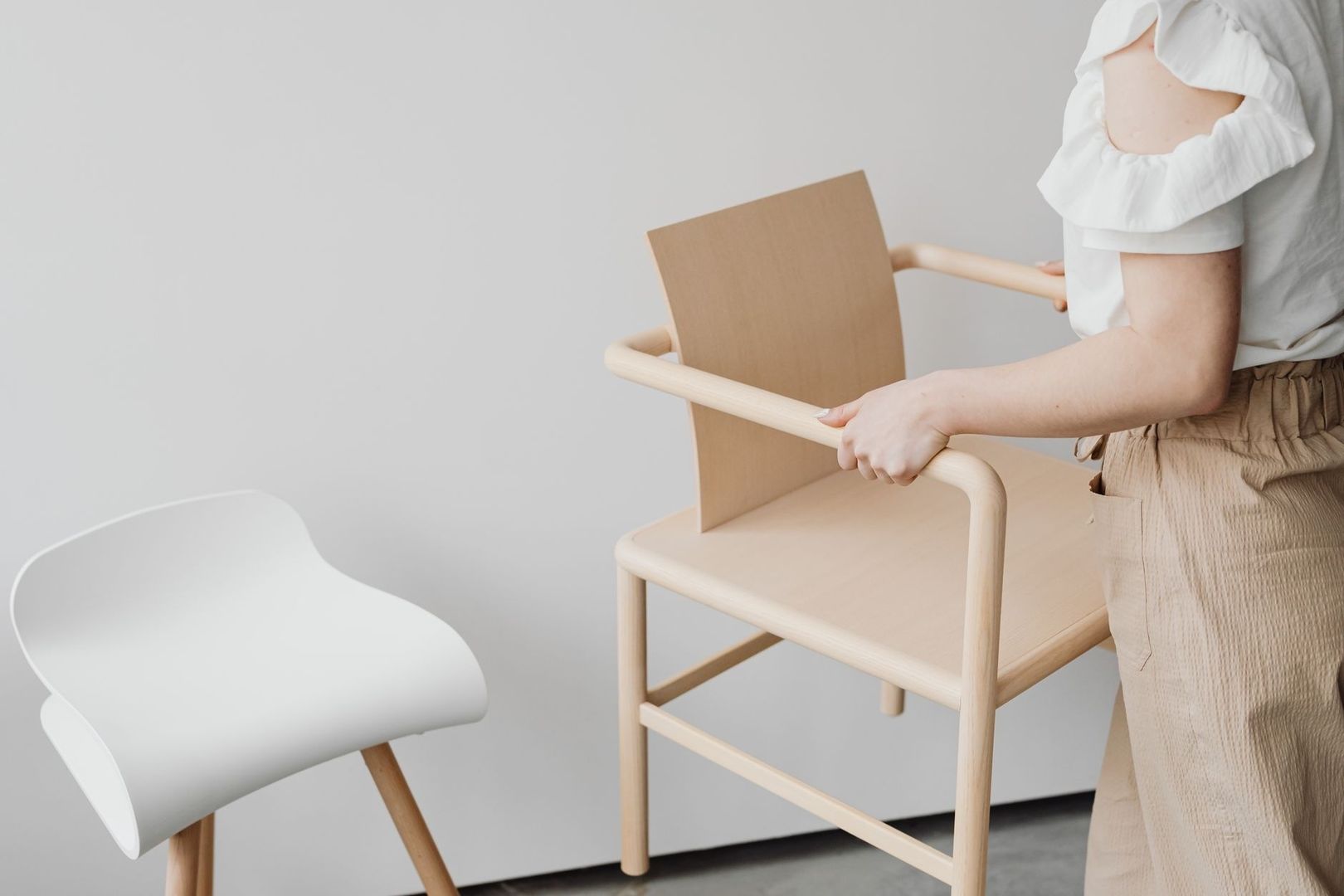 Person bewegt einen minimalistischen Holzhochstuhl neben einem weißen Stuhl